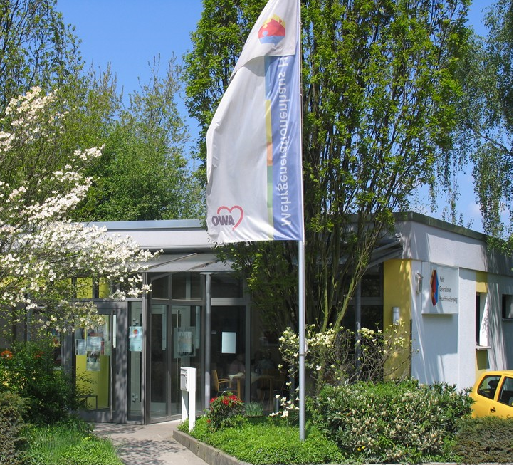 Der Blick auf den Eingang eines modernen Flachdachhauses, umringt von blühenden Büschen.